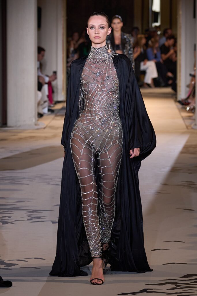A fitted black sequined catsuit paired with a flowing satin cape and high-neck design.