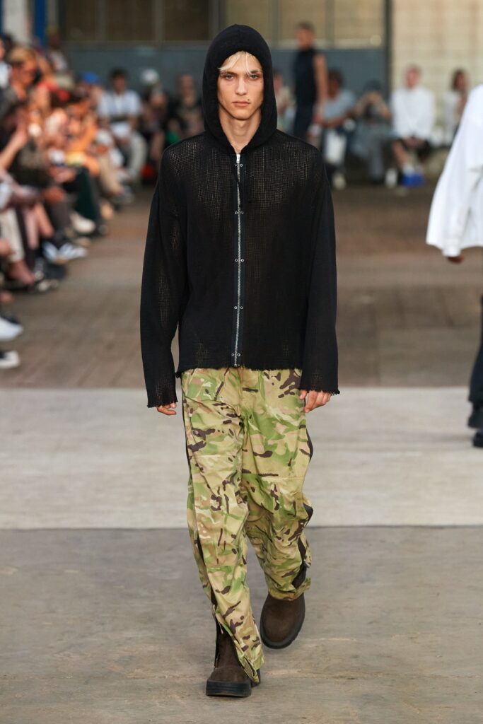 A relaxed black long-sleeve hoodie with a hood paired with camouflage pants.