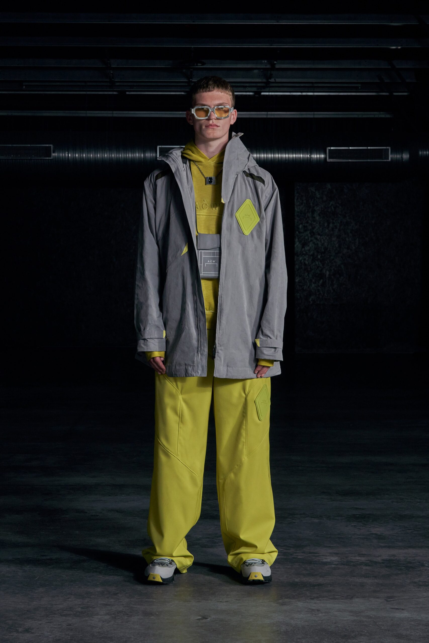 A relaxed gray hooded jacket paired with yellow pants featuring zippered and layered details.