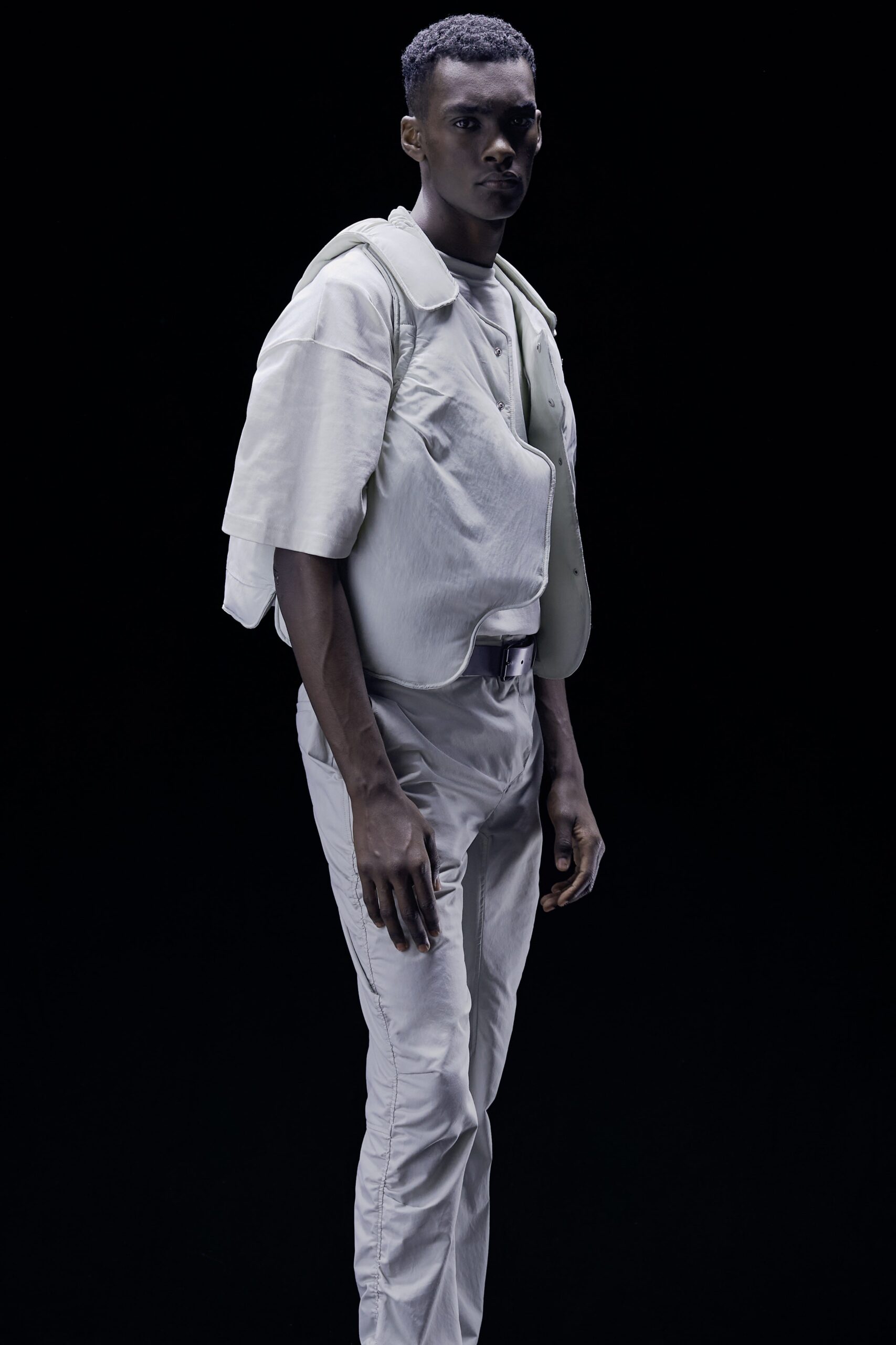 This relaxed ensemble features a short-sleeve jacket with an asymmetric design that adds a contemporary edge. Paired with matching pants, the outfit presents a cohesive look that balances structure and fluidity, creating an intriguing silhouette against a stark backdrop.