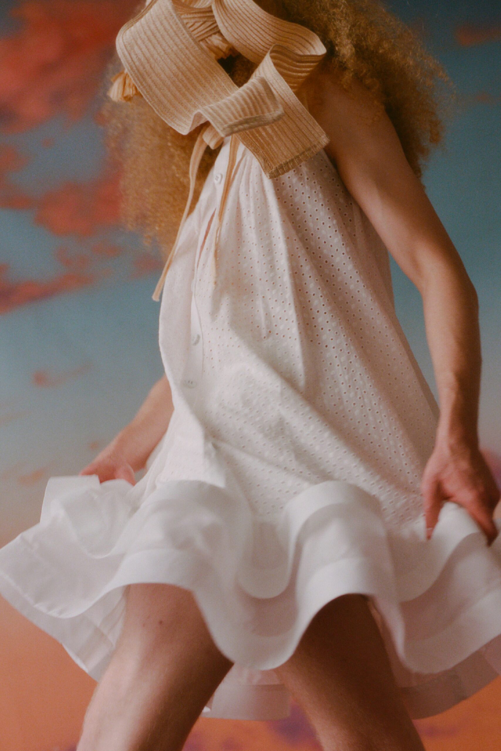 This relaxed sleeveless dress in white features a playful tiered design that adds movement and flow. The V-neckline enhances the lightness of the garment, creating a breezy silhouette that dances with every step.