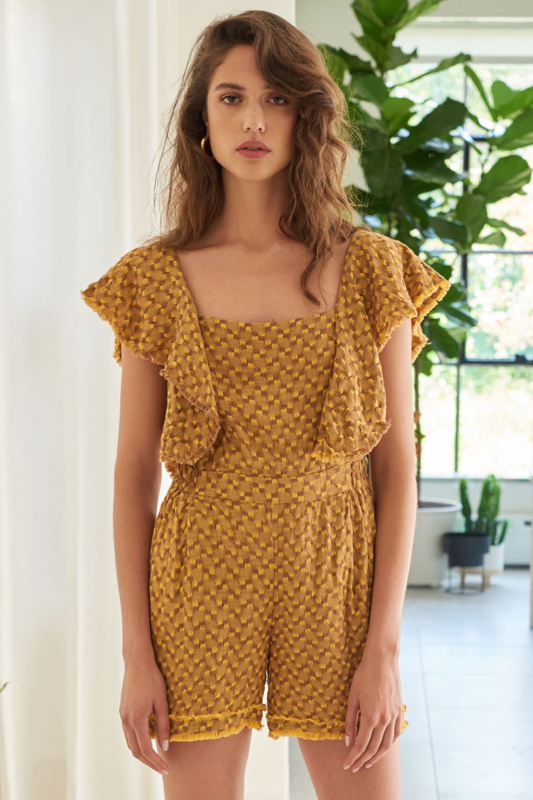 A fitted yellow cotton romper with a square neckline and ruffled sleeves.