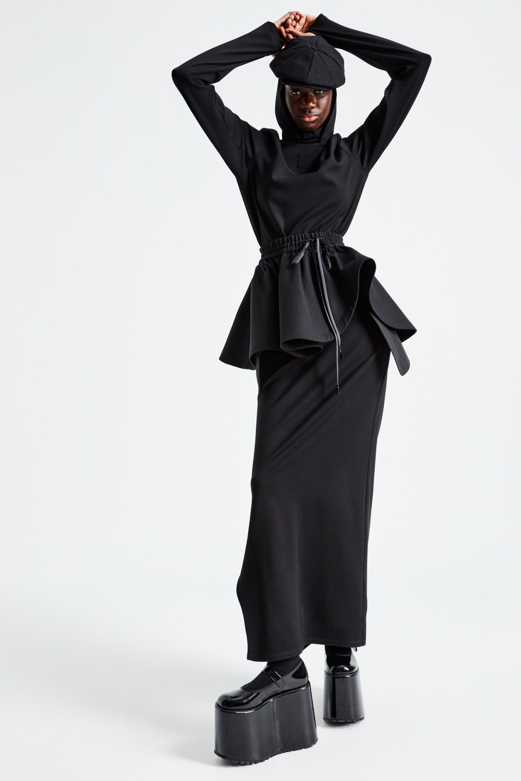 This dress features a fitted silhouette with a striking asymmetric design that adds visual intrigue. The long sleeves and hood create a contemporary edge, while the flowing lower section enhances movement and fluidity.