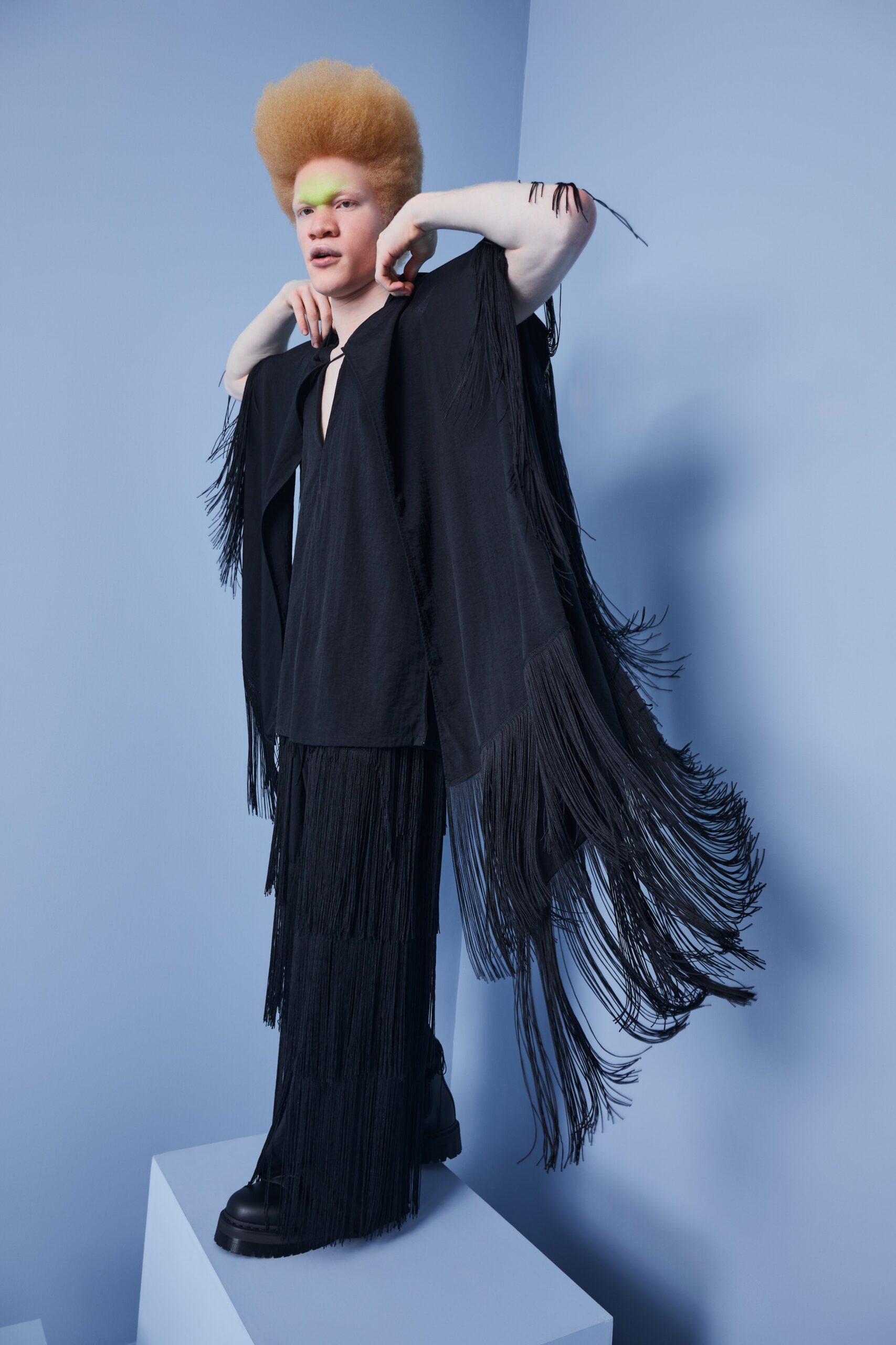 This ensemble features a relaxed black top with dramatic fringe detailing that adds movement and texture. Paired with matching pants, the look creates a striking silhouette that plays with proportions and layers, enhancing the overall visual impact.