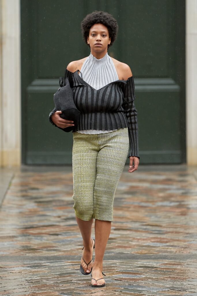 A fitted black striped off-shoulder top paired with high-waisted green pants.