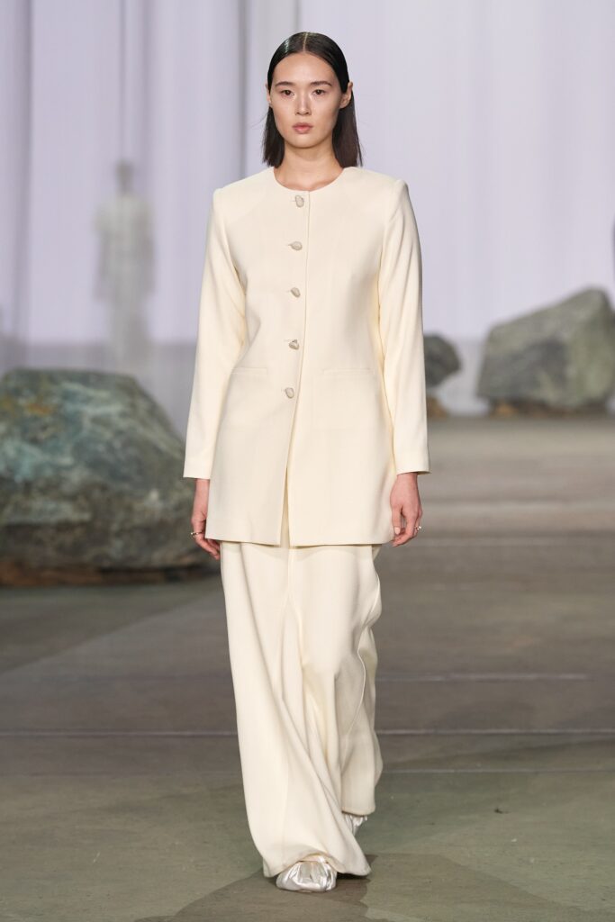 A fitted white jacket with long sleeves and a collared neckline paired with straight-leg pants.