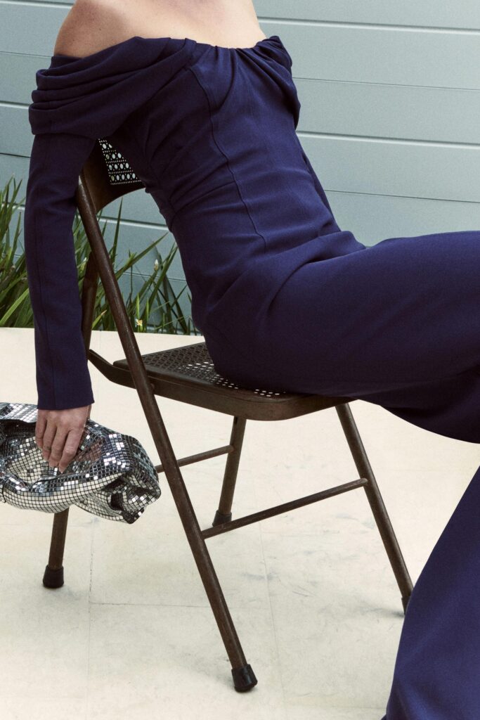 A fitted blue cotton jumpsuit with long sleeves and an off-shoulder design, featuring a straight-leg silhouette.