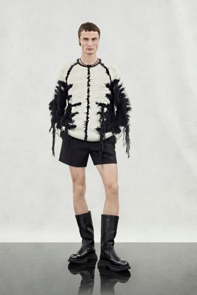 A relaxed black and white sweater with fringed details paired with black shorts.