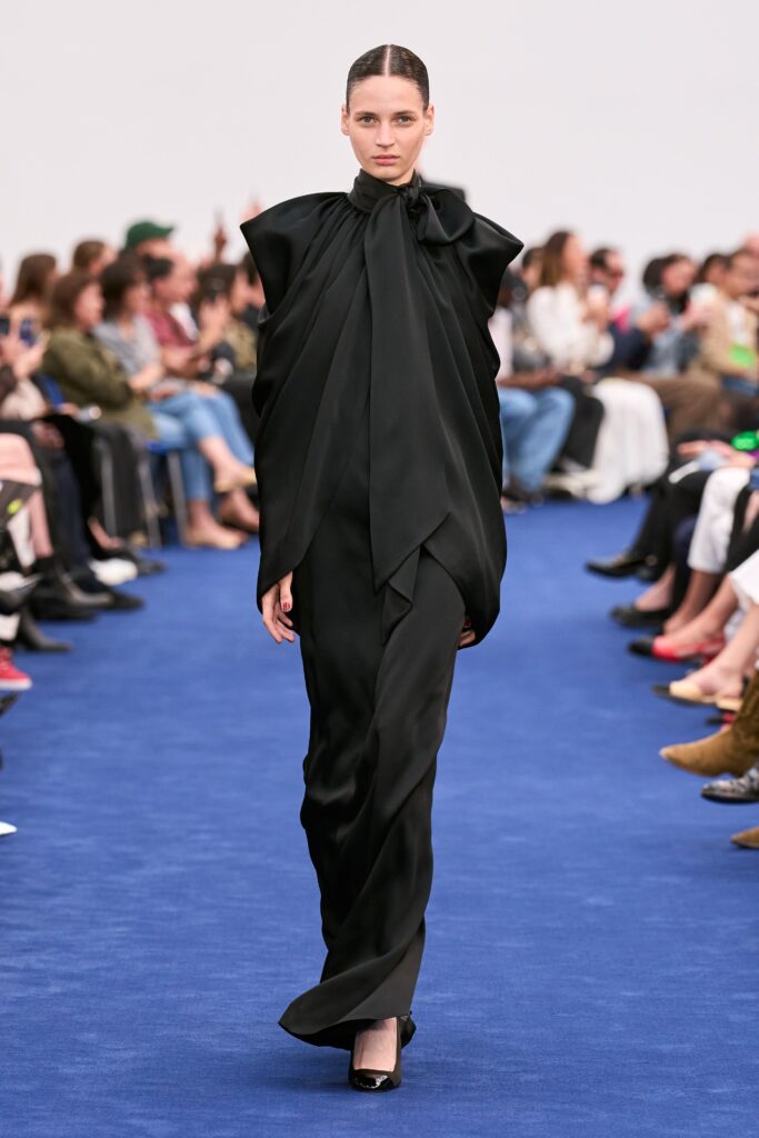 A fitted black silk dress with long sleeves and a high neck, featuring a draped design.