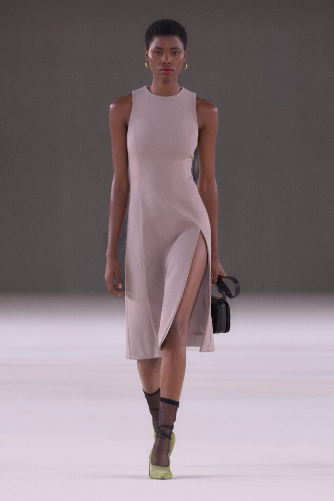 A fitted beige silk dress with a sleeveless design and a high neckline featuring a stylish slit.