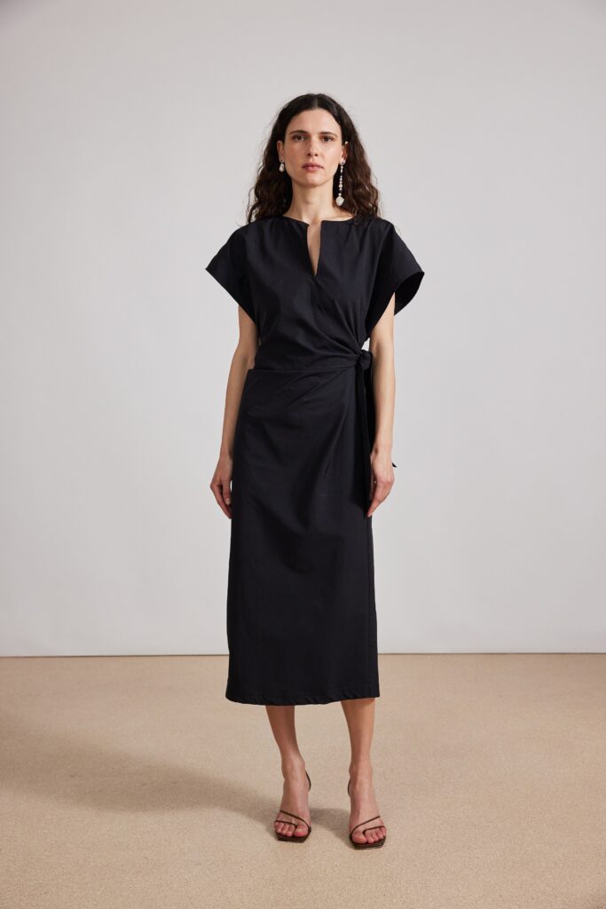 A fitted black cotton dress with a V-neckline and short sleeves, featuring a wrapped design.