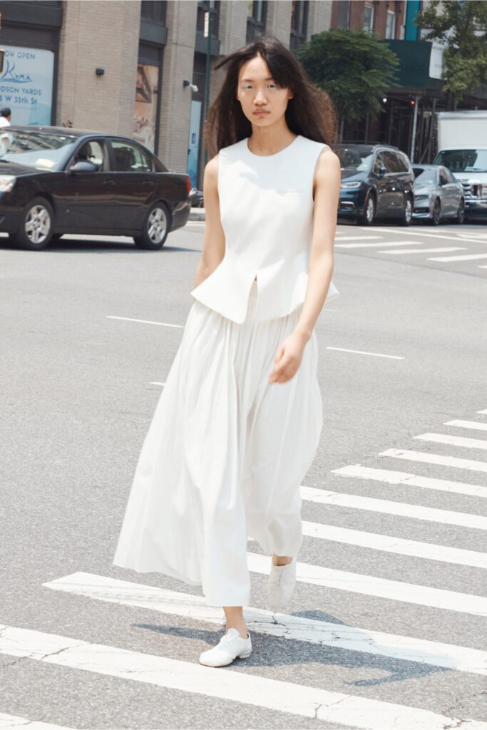 A fitted white sleeveless top paired with a pleated skirt, creating a chic ensemble.
