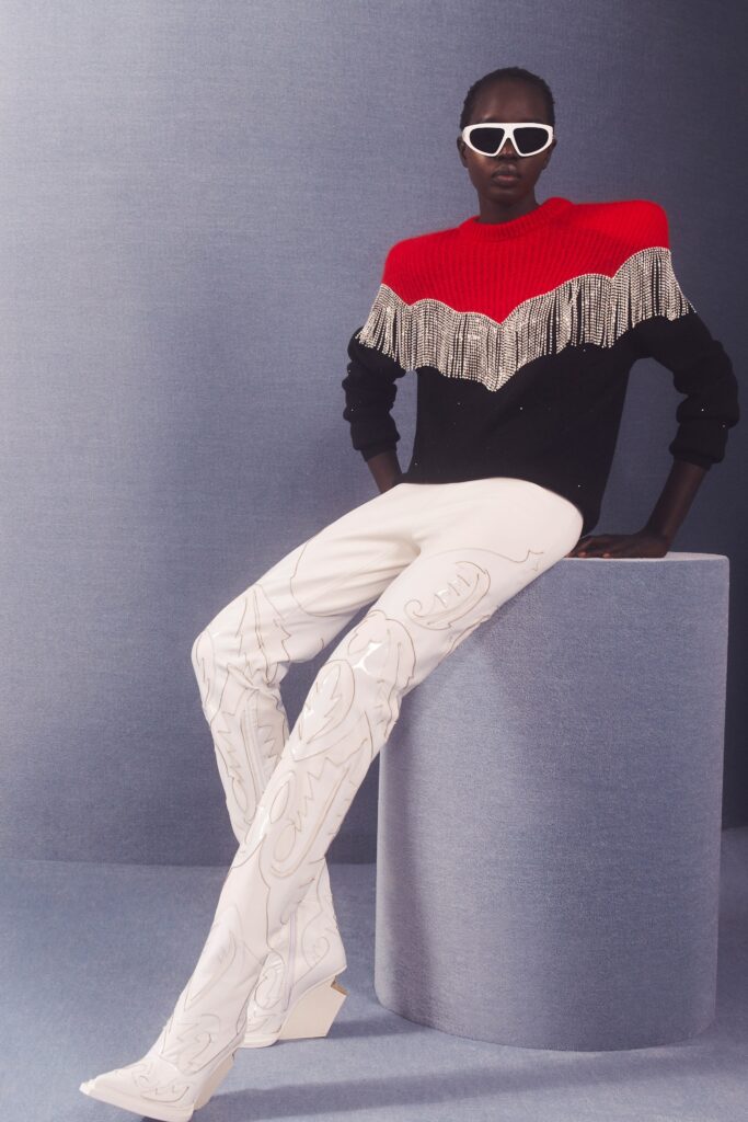 A fitted black and red long-sleeve sweater with fringed details paired with white printed pants.