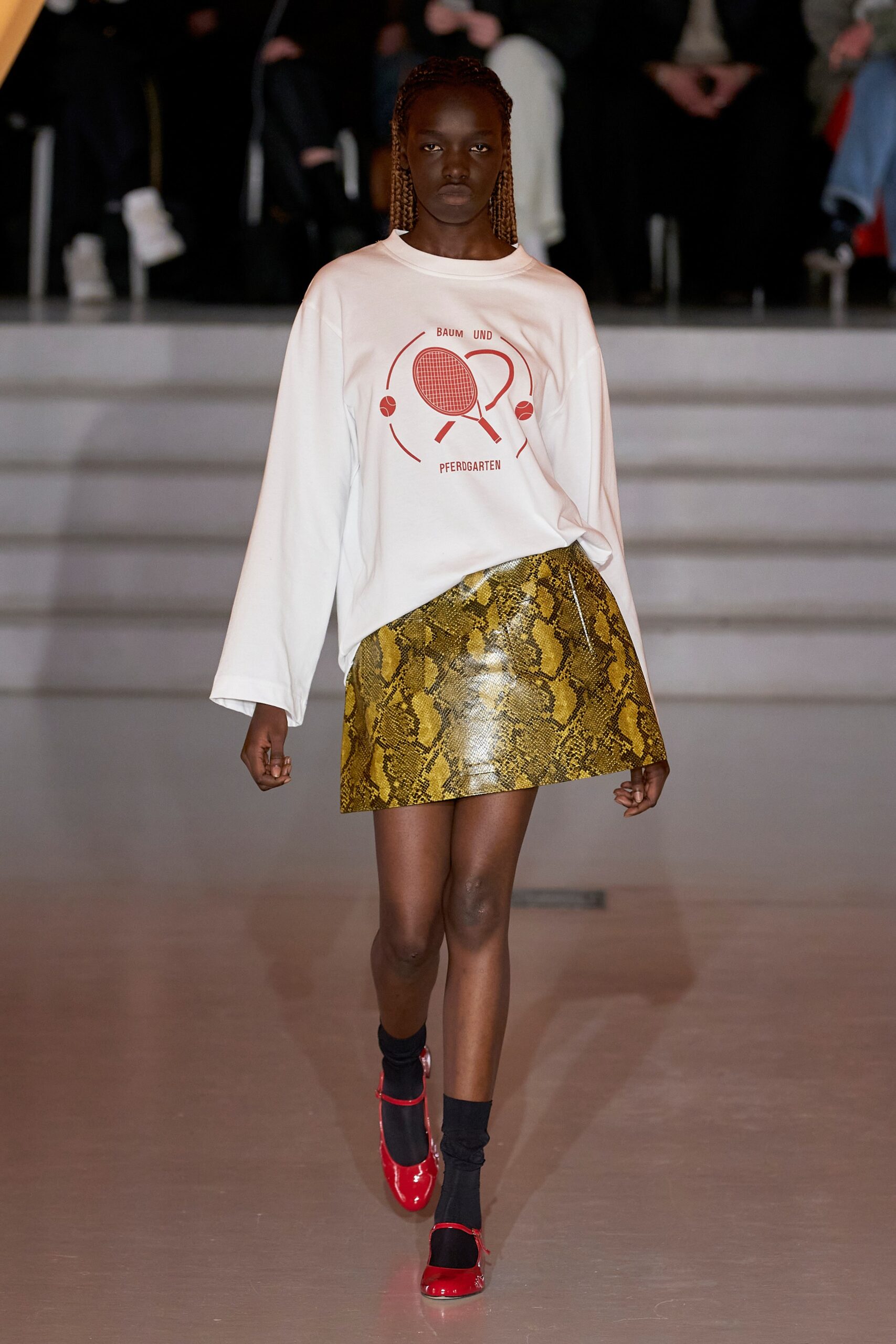 A relaxed white long-sleeve top with a printed design paired with a yellow asymmetric skirt.