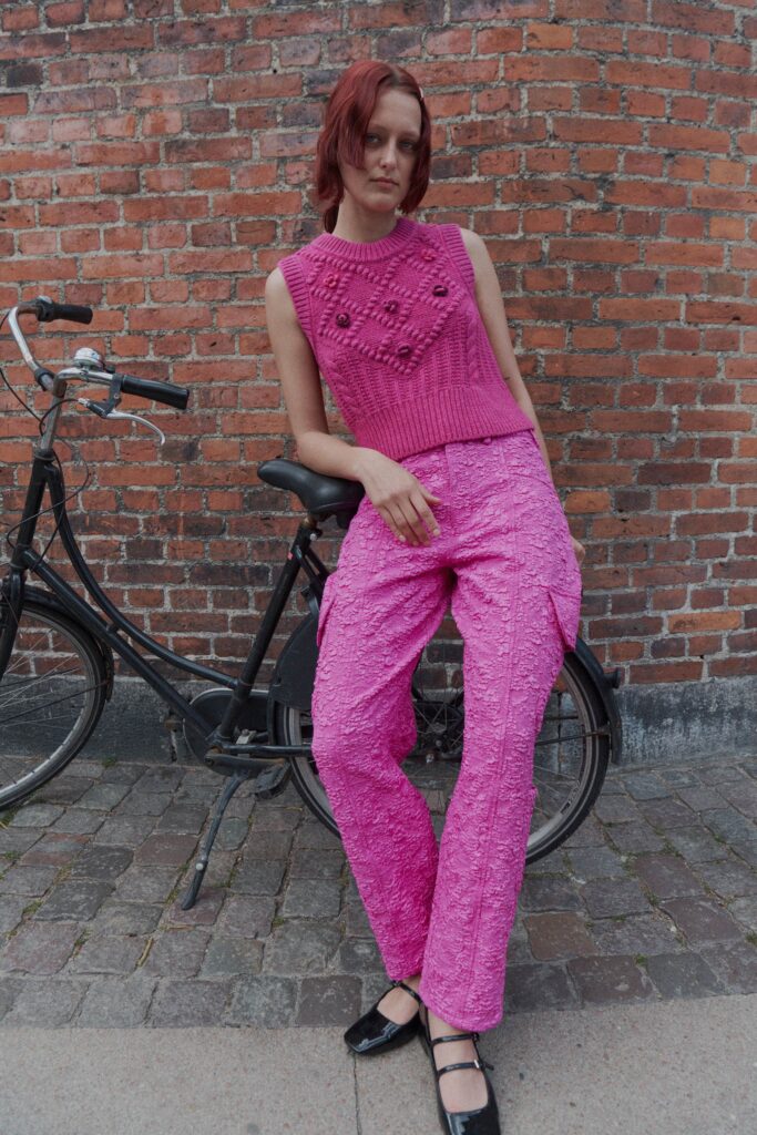A fitted pink sleeveless knit top paired with textured straight-leg pants.