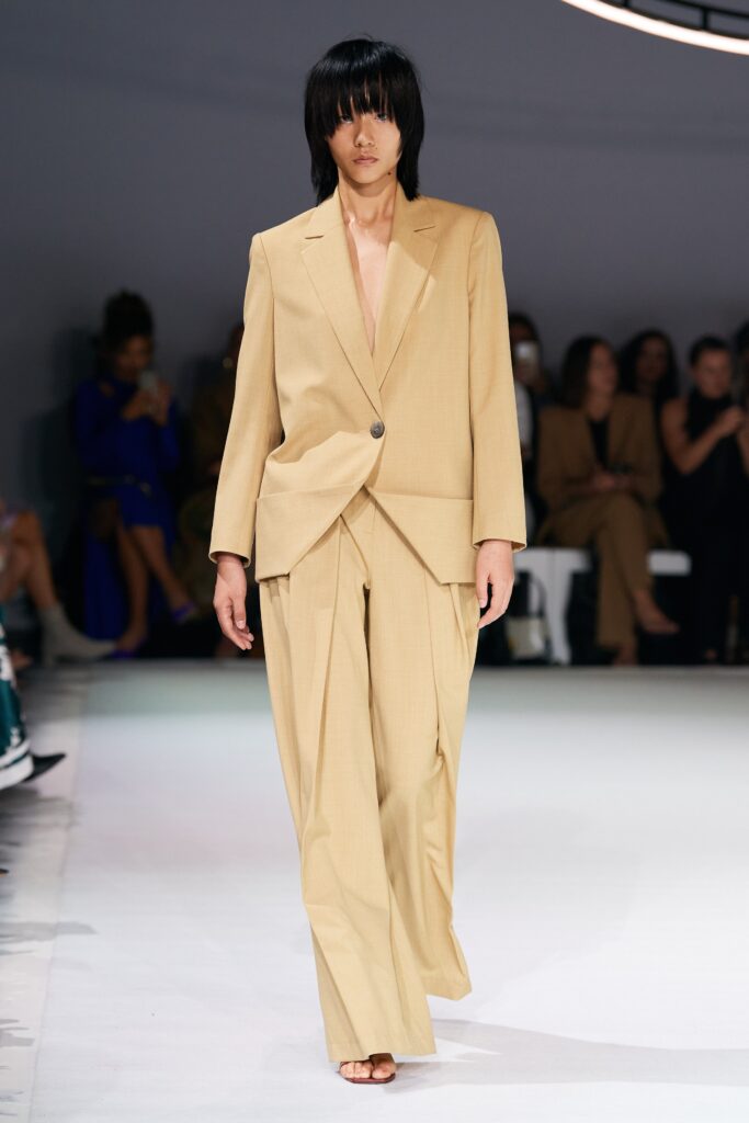 A relaxed beige cotton suit with a collared long-sleeve jacket and wide-leg trousers.
