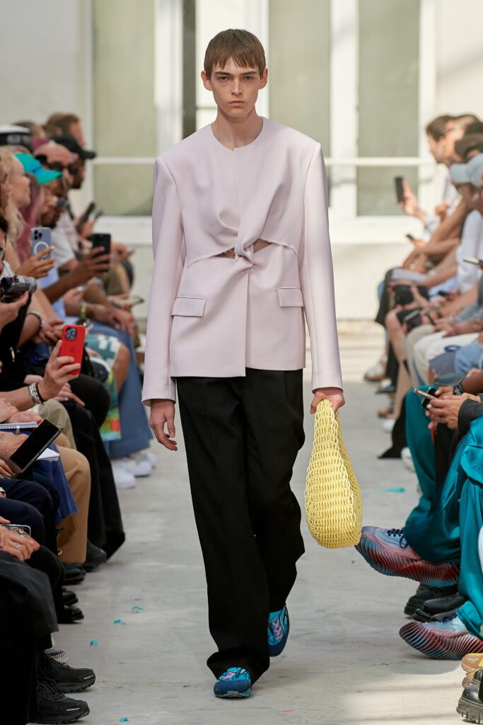 A relaxed pink jacket with an asymmetric design paired with black pants.
