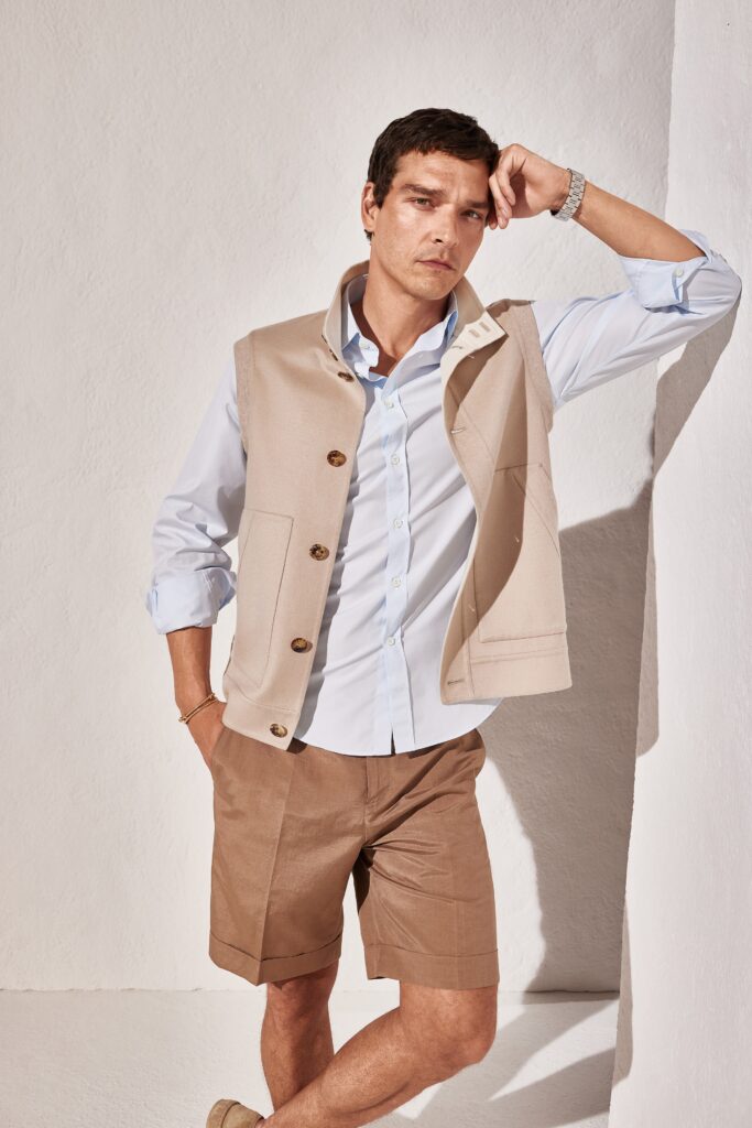 A fitted beige vest layered over a collared blue long-sleeve shirt, featuring button details.