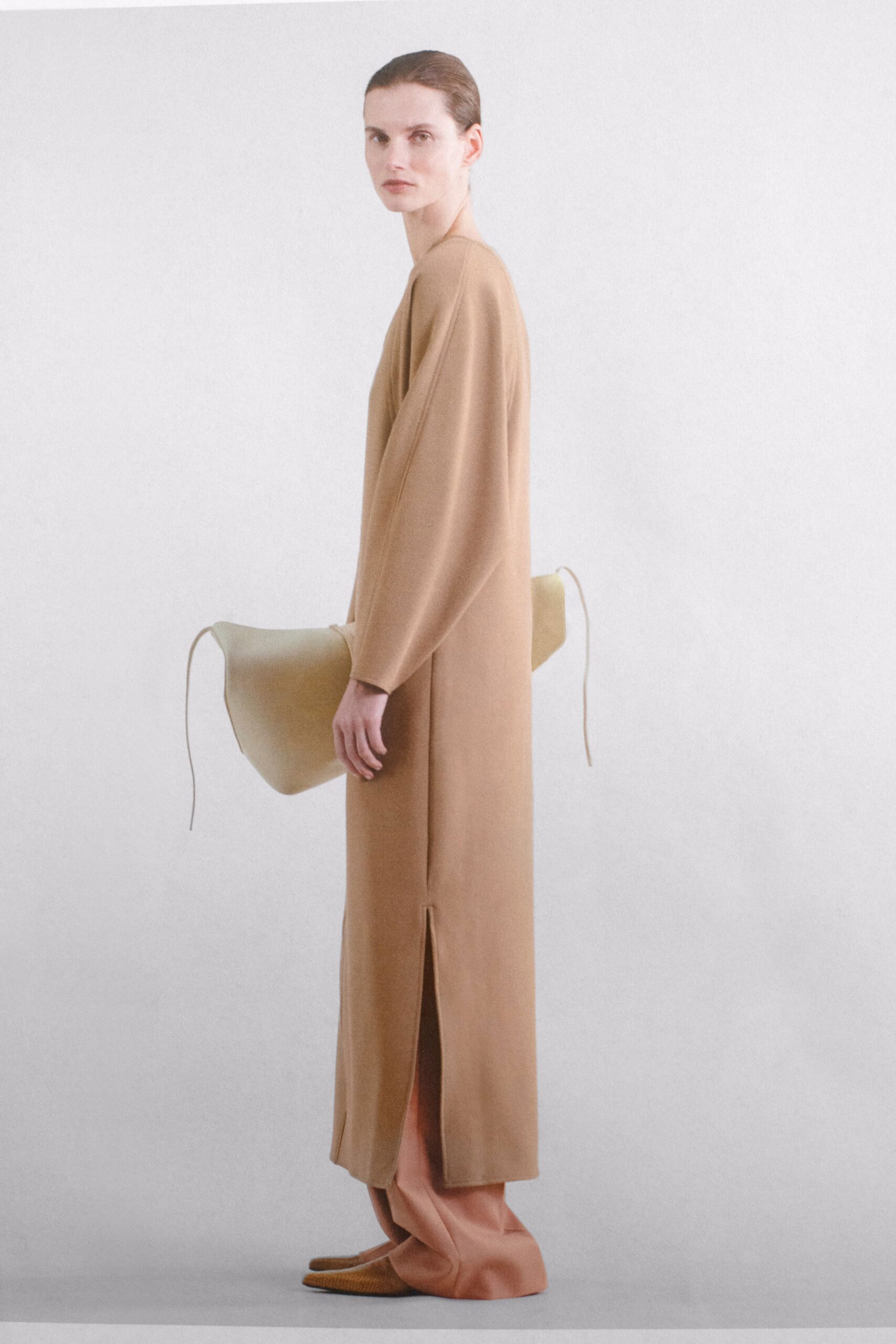 A relaxed beige long-sleeve dress with a high neckline and side slit detail.