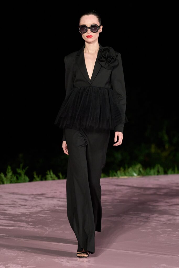 A fitted black jacket with a layered tulle detail and matching pants, featuring a V-neckline.