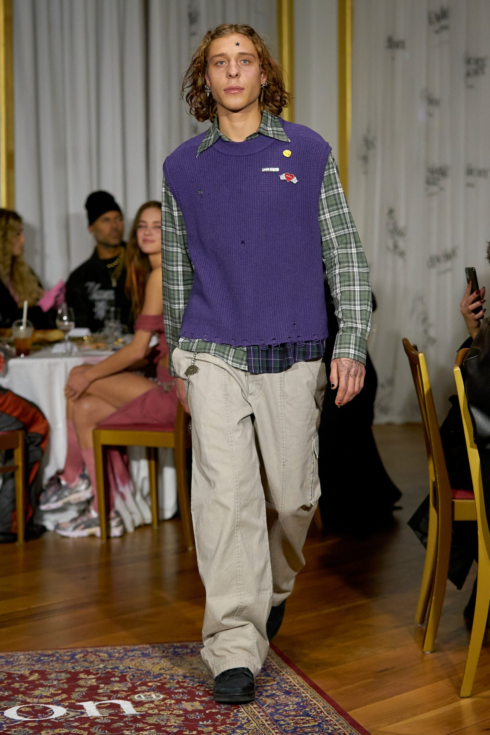A relaxed fit purple cotton sweater layered over a green collared shirt, paired with relaxed pants.