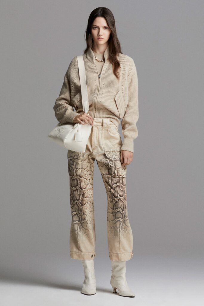 A relaxed beige long-sleeve sweater paired with printed denim pants.