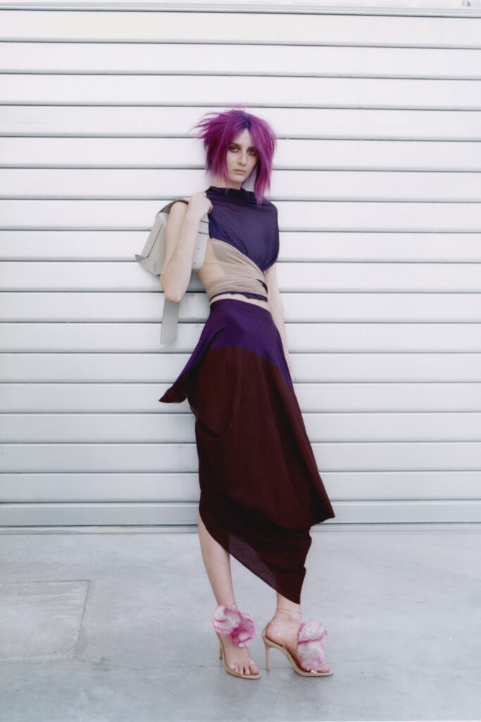 A fitted sleeveless dress with an asymmetric draped design in purple and beige tones.