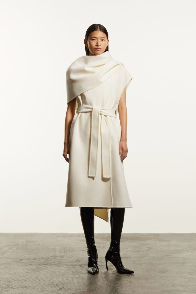 A fitted white wool dress with a high neckline and belted asymmetric design.