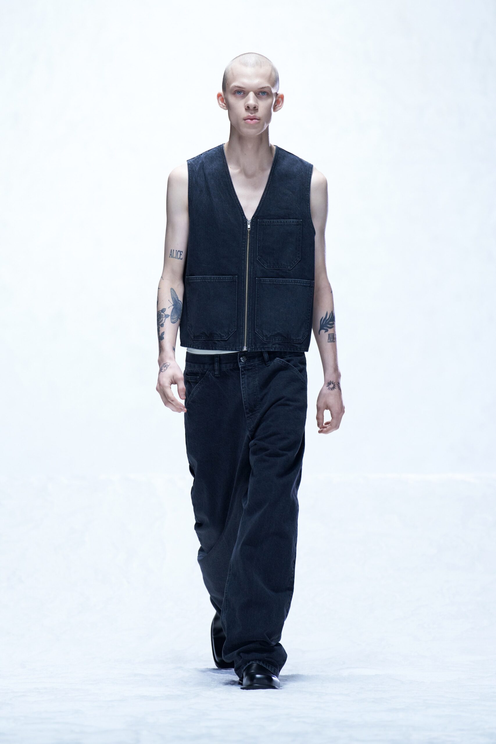 A relaxed black denim sleeveless vest paired with straight-leg pants for a modern look.