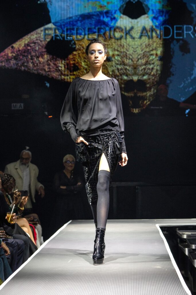 A fitted black silk off-shoulder dress with long sleeves and an asymmetric slit detail.