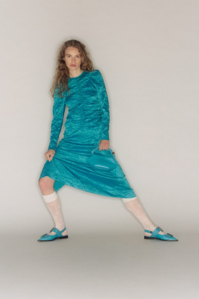 A fitted blue silk dress with long sleeves and a V-neckline featuring a ruched design.