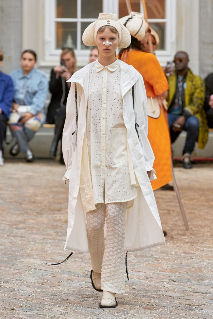 A relaxed white coat dress with long sleeves and a collared neckline, featuring layered design details.