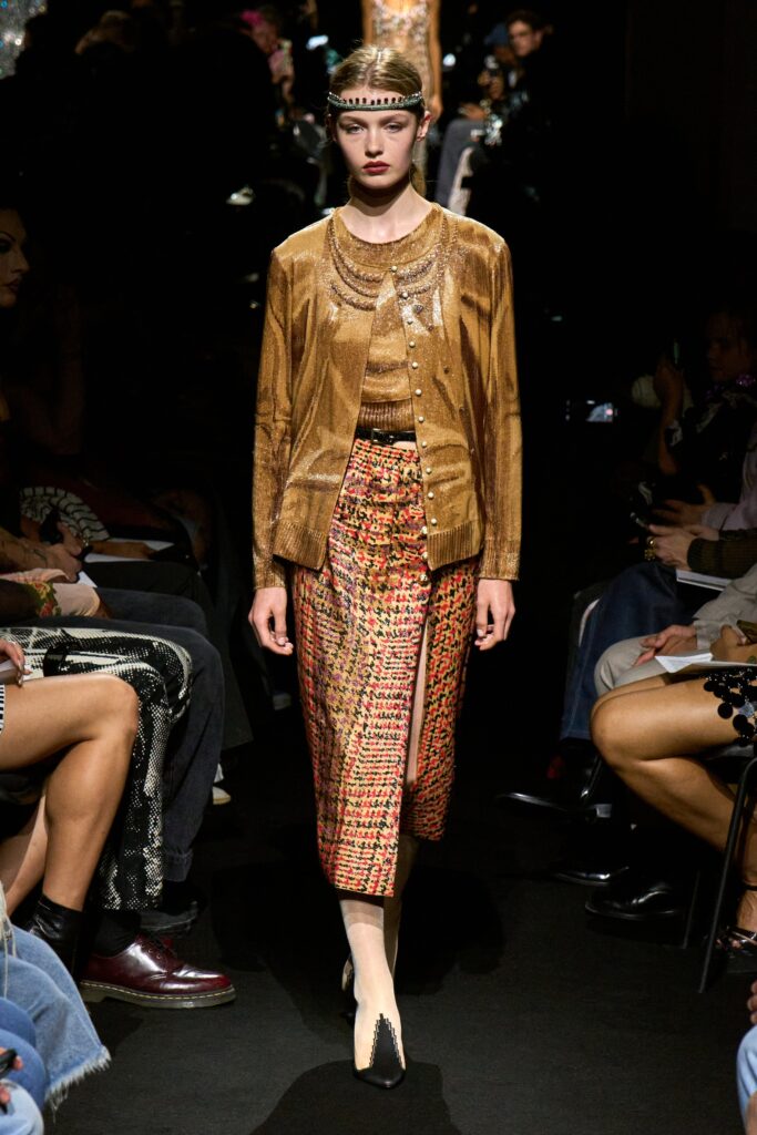 A fitted gold silk cardigan paired with a layered asymmetric skirt featuring red accents.