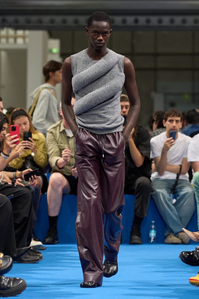 A fitted gray sleeveless top with an asymmetric design paired with burgundy leather pants.