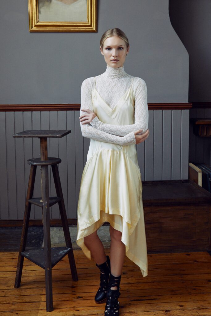 A fitted cream silk sleeveless dress with a V-neckline and asymmetric hemline.