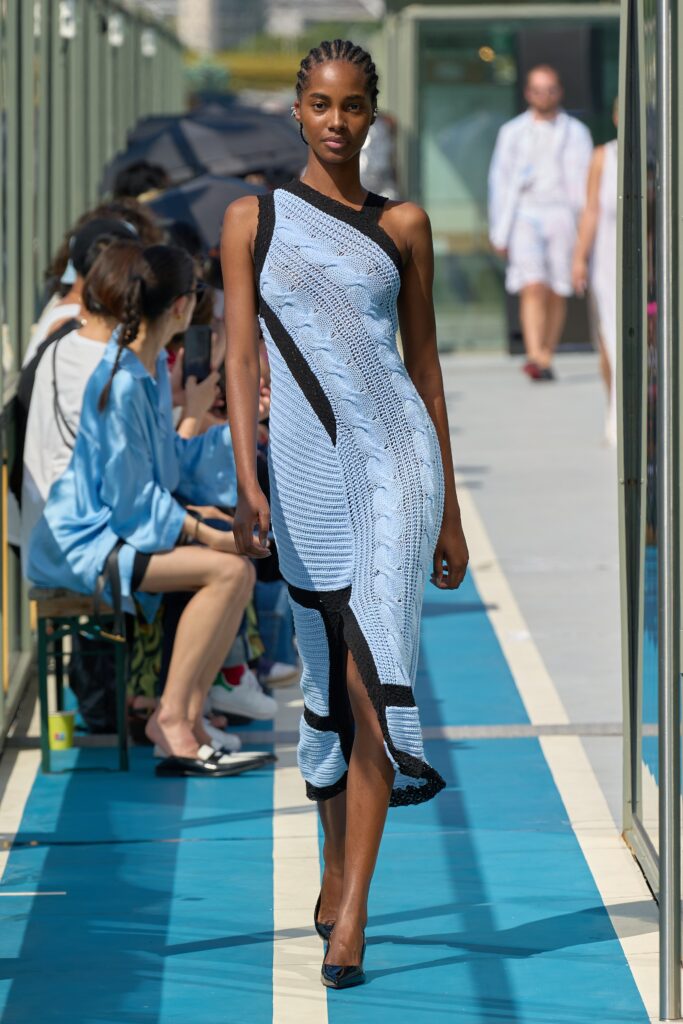 A fitted blue knit dress with an asymmetric design and layered details.