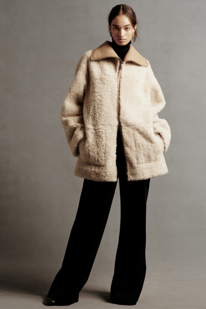 A relaxed beige fur coat paired with black pants featuring a collared neckline and zippered closure.