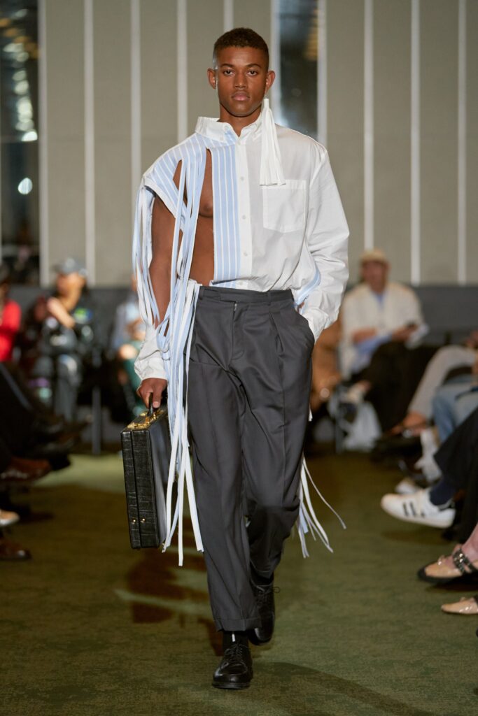A relaxed white cotton shirt with long sleeves, fringed details, and gray pants.