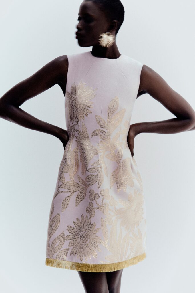 A fitted pink silk sleeveless dress with a high neckline and embroidered flared design.