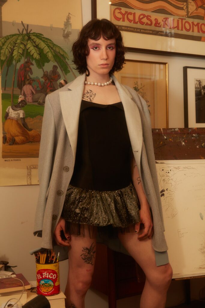 A fitted black sequined dress layered under a gray collared jacket with an asymmetric silhouette.