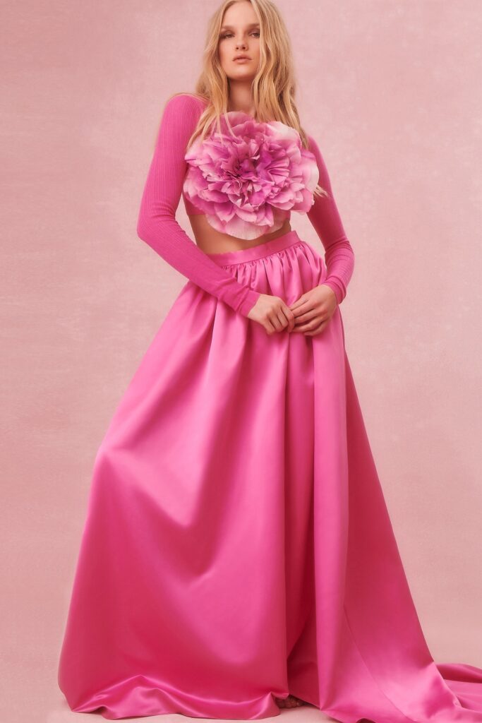 A fitted pink silk top with long sleeves and a pleated skirt, featuring a floral detail.