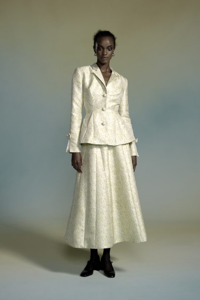 A fitted yellow silk blazer with long sleeves and a pleated flared skirt.
