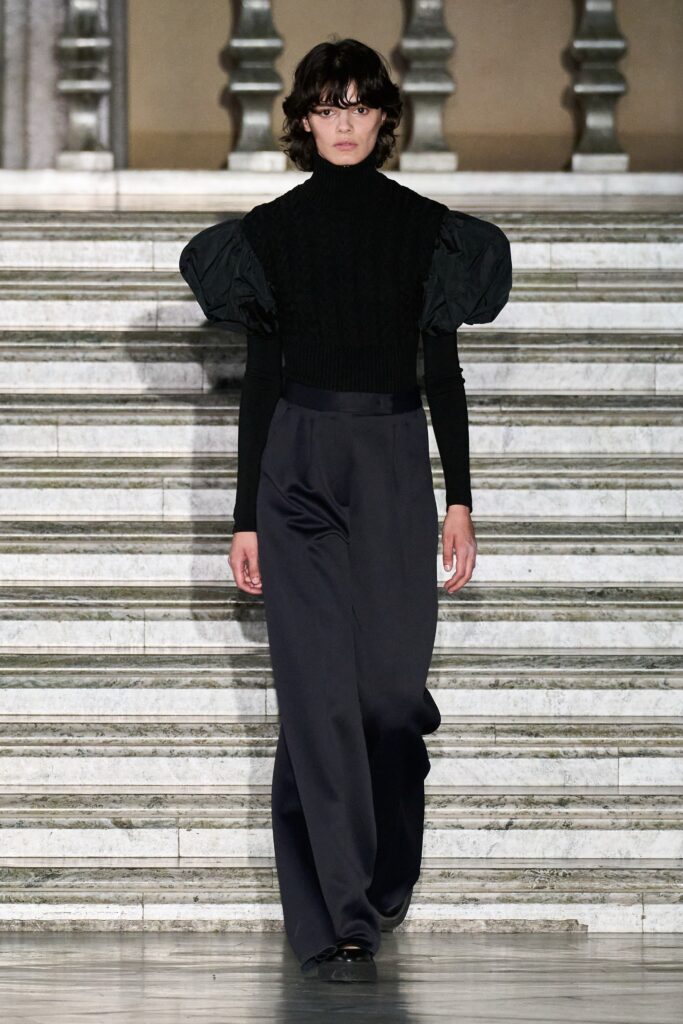 A fitted black long-sleeve top with puffed sleeves paired with wide-leg black pants.
