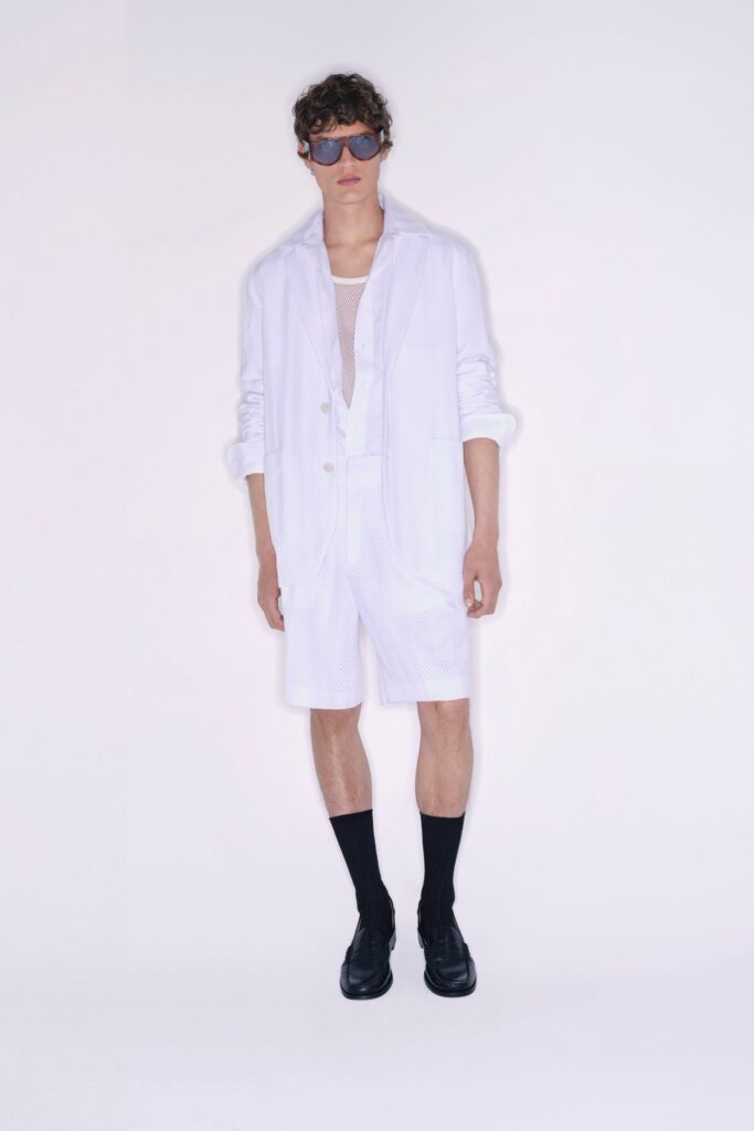A relaxed white jacket with long sleeves and collared design paired with pleated shorts.