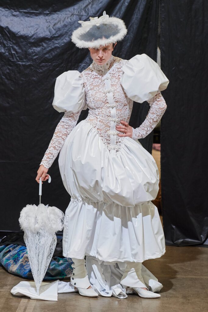 A fitted white lace dress with long sleeves and a high neckline featuring a tiered silhouette.