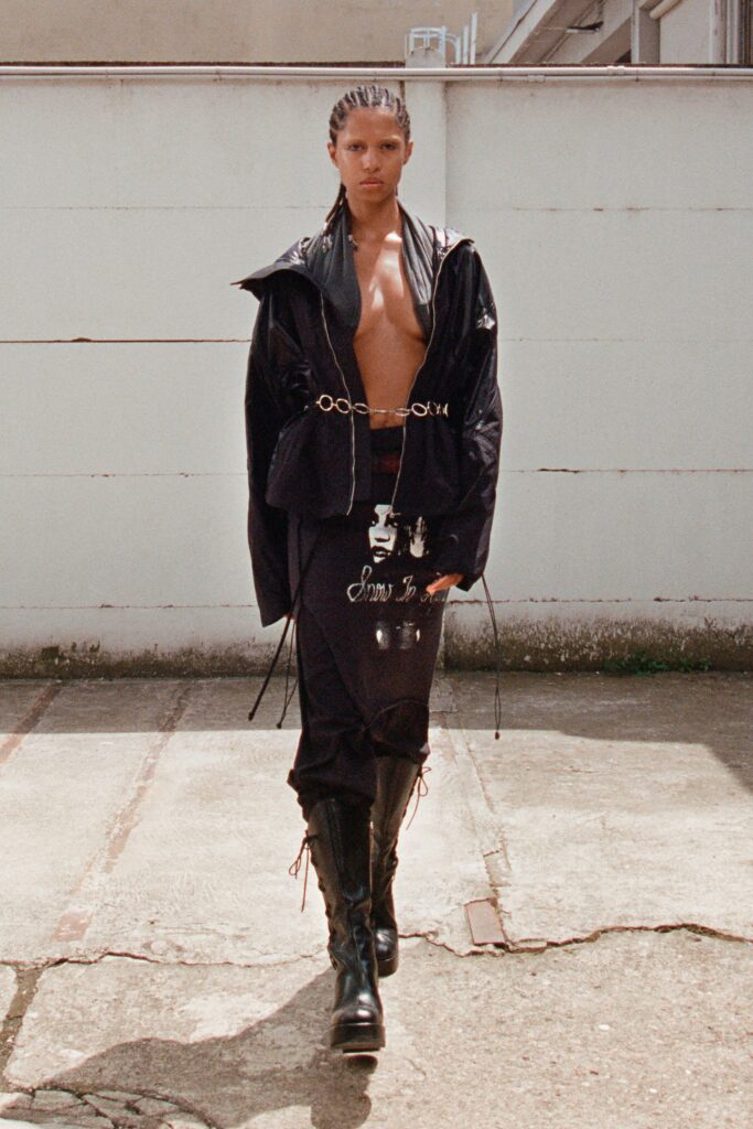 A fitted black leather jacket with long sleeves and an asymmetric zippered skirt.