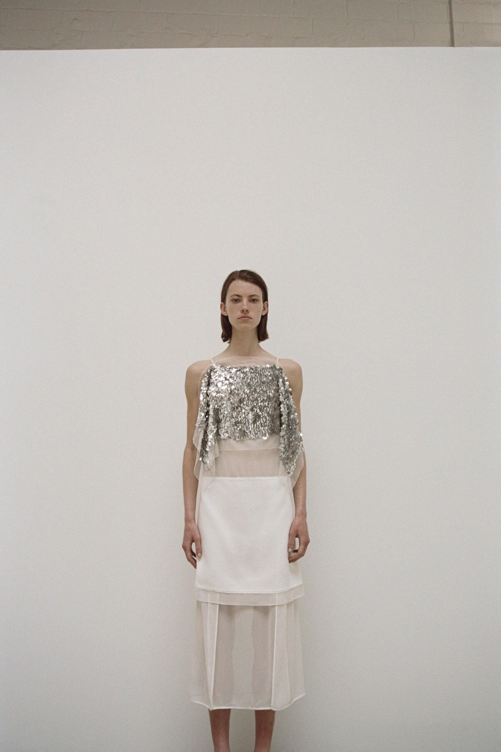 A fitted white silk dress with a sleeveless high-neck design and layered details.