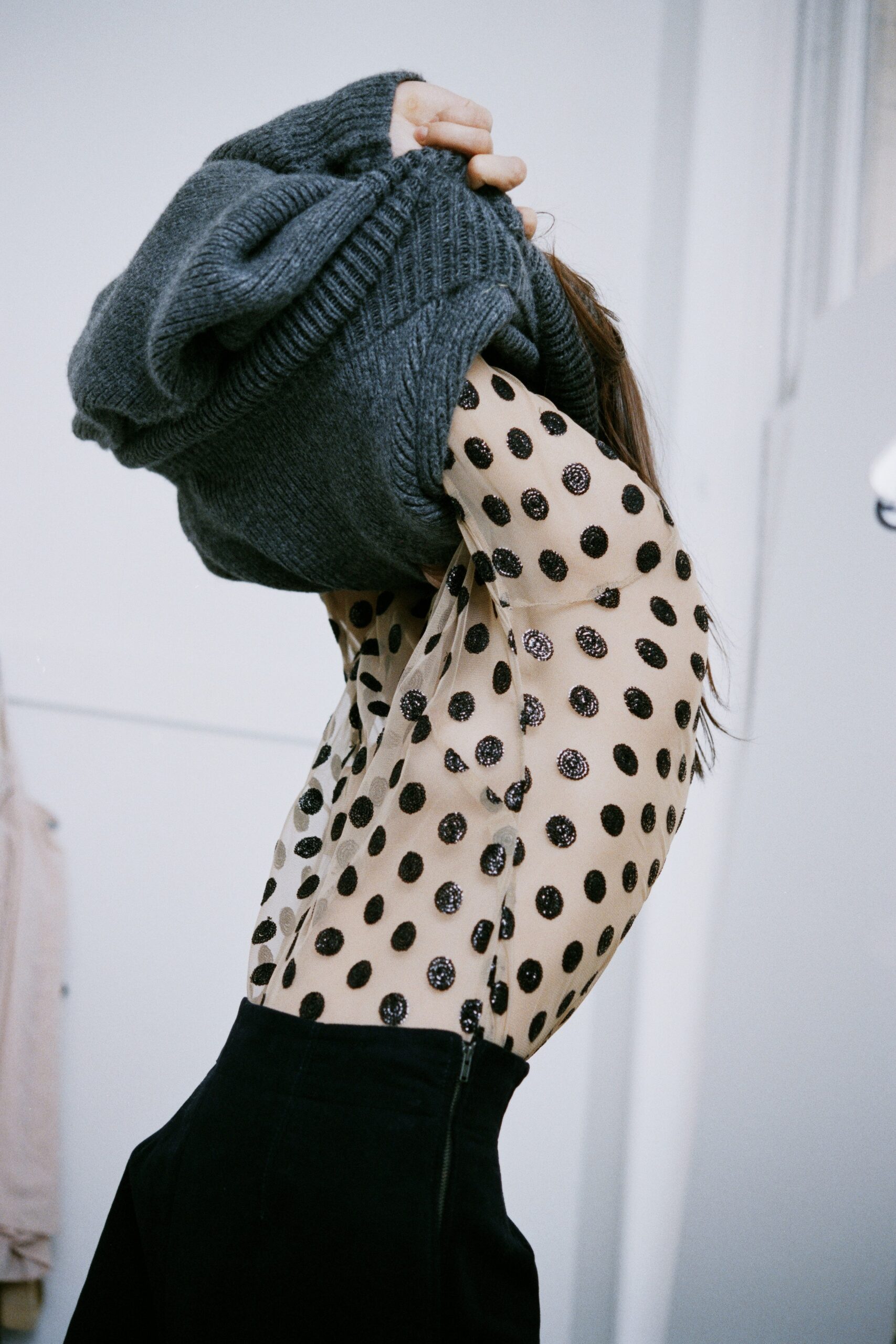 A fitted beige polka-dot top with long sleeves paired with black fitted pants.