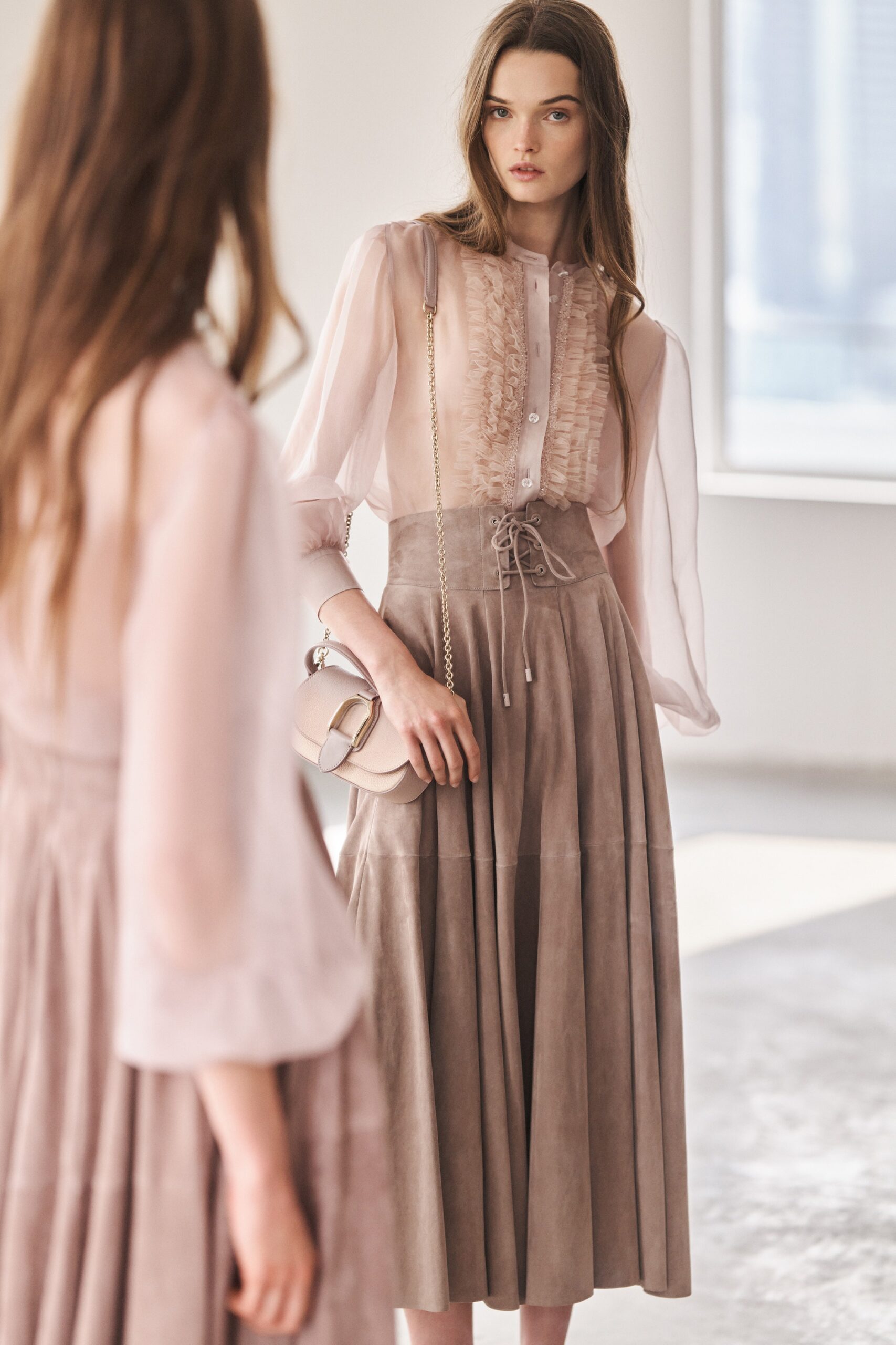 A fitted beige silk blouse with long sleeves and a pleated tiered skirt.