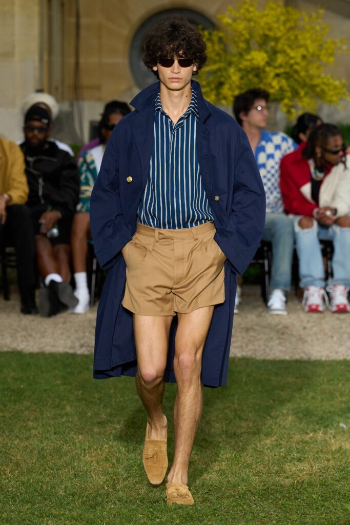 A relaxed blue striped long-sleeve shirt paired with a tan coat and shorts.